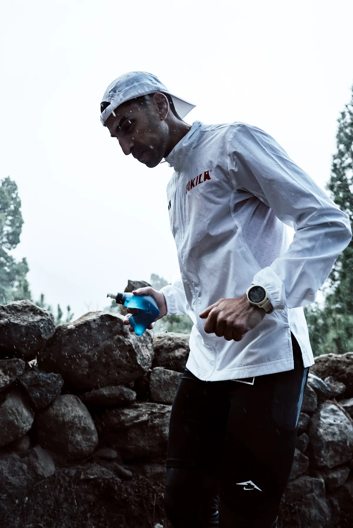 Corredor de trail junto a un muro de piedra bajo la lluvia
